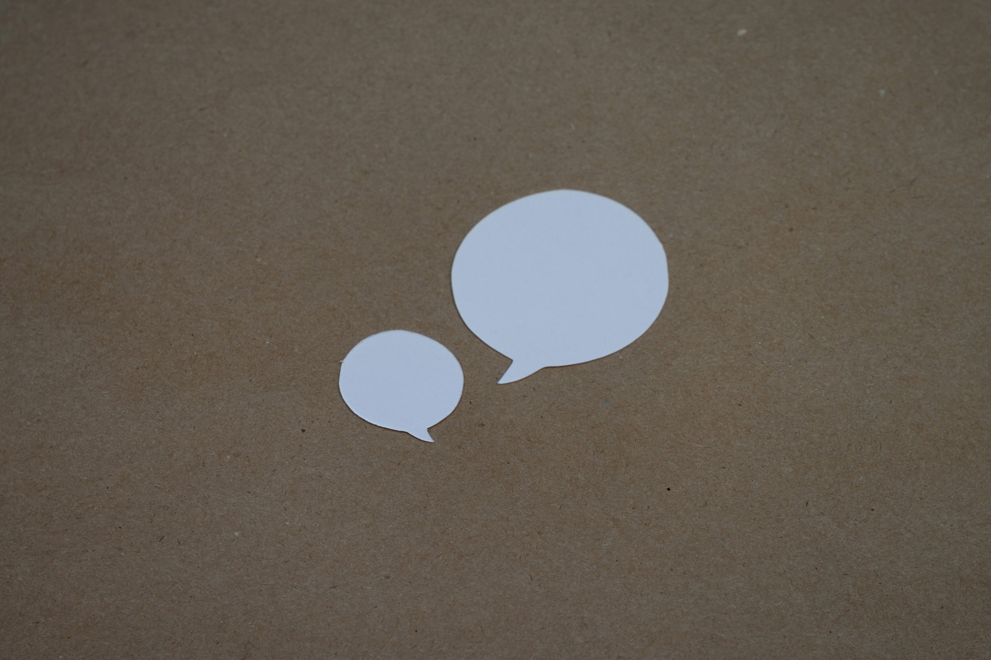 two-white-speech-bubbles-sitting-on-top-of-a-brown-surface.jpg two white speech bubbles sitting on top of a brown surface